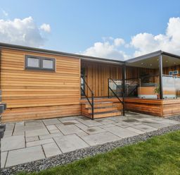 A wooden lodge with stairs leading to a covered deck area with glass railings at Enia Lodge 2 Llanelidan near Corwen