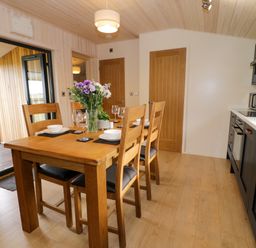A kitchen dining area with a wooden table set for four with flowers and glassware at Enia Lodge 2 Llanelidan near Corwen