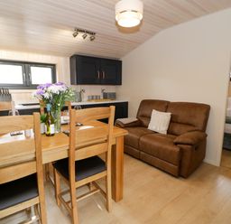A dining area with wooden table and chairs next to a brown sofa and kitchen cabinets in Enia Lodge 2 Llanelidan near Corwen