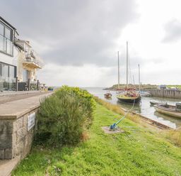 A waterfront with boats moored near a building and a grassy bank at Lazey Cottage in Haverigg