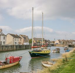 A canal with several boats moored along the banks and houses lining the opposite side at Lazey Cottage in Haverigg