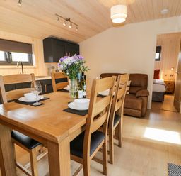 A dining area with wooden table and chairs set with plates glasses and flowers next to a kitchen with black cabinets at Math Lodge 3 Llanelidan near Corwen