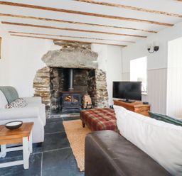 A living room with a wood burning stove in a stone fireplace two sofas a wooden side table and a television on a wooden cabinet at Hilldene in Treknow