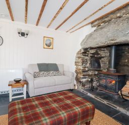 A living room with a stone fireplace and a wood burning stove a plaid ottoman a beige sofa and two round mirrors on the wall at Hilldene in Treknow