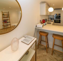 A kitchen with a white countertop and wooden bar stools next to a table with a clear vase and plates at Amelia's Point in St Ives