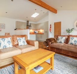 A living room with two brown sofas, a wooden coffee table, a kitchen area, and a rug at 10 Water's Edge in Lanreath