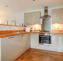 A kitchen with wooden countertops a stainless steel oven and range hood and light-colored cabinets at 10 Waters Edge in Lanreath
