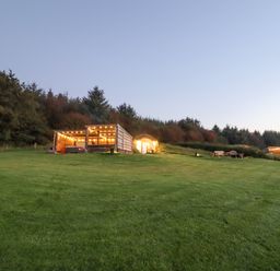 A grassy lawn with a wooden pergola and a round door building set into a hillside with trees in the background at Rhosydd in Cyffylliog near Ruthin