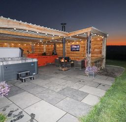 An outdoor covered patio area with a hot tub wood stove seating and a television at Rhosydd in Cyffylliog near Ruthin