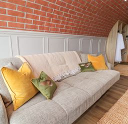 A gray sofa with yellow and green cushions in a room with brick curved wall and wooden door at Cae Bach in Cyffylliog near Ruthin