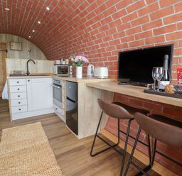 A kitchen area with white cabinets and wooden countertops next to a wooden bar with a television and two stools at Cae Bach in Cyffylliog near Ruthin