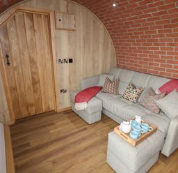 A living room with a gray sofa and ottoman with a wooden tray of cups in a room with brick and wood walls at Weirglodd in Ruthin