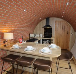 A kitchen with a curved brick ceiling a wooden countertop with four place settings and bar stools at Weirglodd in Ruthin