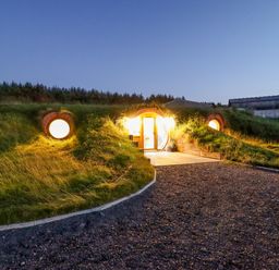 A grass covered earth house with round windows and a lit entrance at Weirglodd in Ruthin