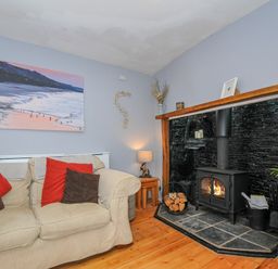 A living room with a beige sofa and cushions near a black wood stove with a wooden mantle at Stone's Throw Cottage in Launceston