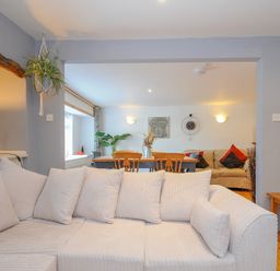 A living room with a white sofa wooden dining table and chairs and a plant at Stone's Throw Cottage in Launceston
