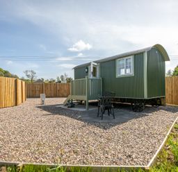 A small green tiny house on wheels with a fenced gravel yard and two black chairs at Strathmore in Burnside near Forfar