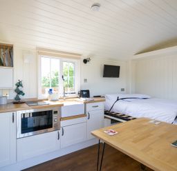 A compact kitchen and sleeping area with a bed a microwave a sink and a table at Strathmore in Burnside near Forfar