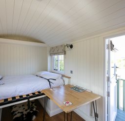 A small room with a single bed a wooden table an open door and a window at Strathmore in Burnside near Forfar