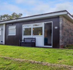 A small single-story house with dark wood siding and stone wall on a grassy slope at Florence's Nest in Dartmouth