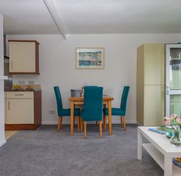 A dining room with a wooden table and teal chairs and a living area with a white coffee table and a gray sofa at Florences Nest in Dartmouth