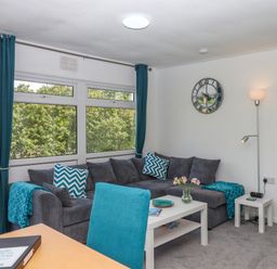 A living room with a gray sofa blue cushions a white table a floor lamp and a wall clock at Florences Nest in Dartmouth