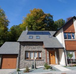 A house with stone and wood exterior with solar panels on the roof surrounded by trees at The Arthouse in Ambleside