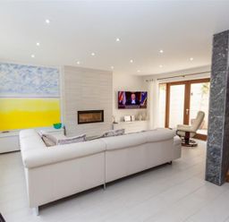 A living room with a white sectional sofa a fireplace and a television near wooden doors at The Arthouse in Ambleside