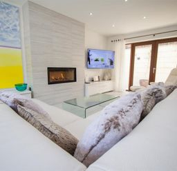 A living room with a fireplace wall mounted tv glass coffee table and white sofa with cushions at The Arthouse in Ambleside