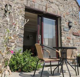 A stone patio with two wicker chairs and a round table outside a building with glass double doors at Carreg Ddu in Solva