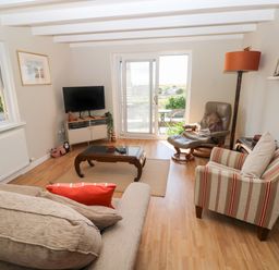 A living room with a sofa, armchair, coffee table, TV, floor lamp, and sliding glass door at Carreg Ddu in Solva