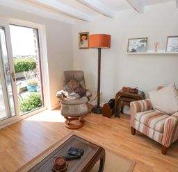 A living room with a brown leather chair and striped armchair next to a floor lamp and glass door at Carreg Ddu in Solva