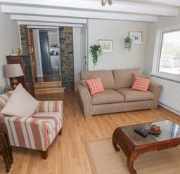 A living room with a striped armchair a beige sofa two shelves with plants and pictures and a wooden coffee table at Carreg Ddu in Solva