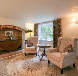 A sitting room with two upholstered armchairs a wooden side table an arched brick fireplace and a window with curtains at West View in Feltwell