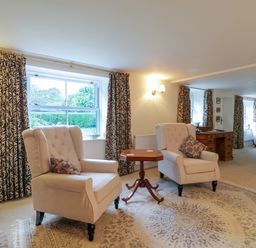 A sitting area with two armchairs and a small table in front of windows with patterned curtains at West View in Feltwell