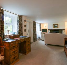 A living room with wooden desk, patterned curtains, white sofas, fireplace, and a television at West View in Feltwell