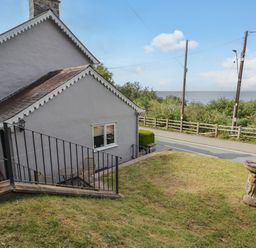 A grassy yard with a birdbath and a white house near a road with a view of the sea