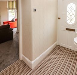 A hallway with striped carpet a white door and a small round table with flowers and a view into a living room with a brown sofa and an orange sofa at Morva in New Quay