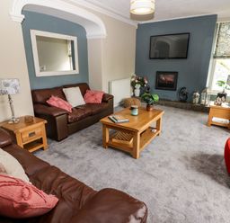 A living room with brown leather sofas a wooden coffee table a wall-mounted television and a fireplace at Morva in New Quay