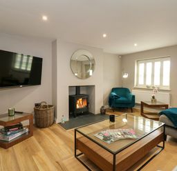 A living room with a wall-mounted TV a fireplace with a round mirror a blue armchair wooden tables and a glass coffee table at Daisy's Place South Creake near Little Walsingham