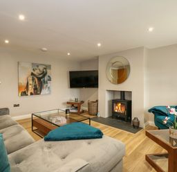 A living room with a gray sectional sofa teal pillows a glass coffee table a fireplace and a wall-mounted television at Daisys Place in South Creake near Little Walsingham