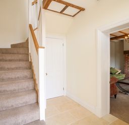 A stairway with carpeted steps and a wooden handrail next to a closed white door and an open doorway leading to a living room with a glass coffee table at Daniels Farmhouse in Claines