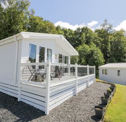 A white mobile home with chairs on a deck and a row of plant pots along a gravel path at Bethany's Retreat in Wemyss Bay