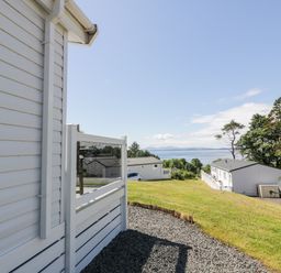 A view of white houses on a grassy hill with trees and water in the background at Bethany's Retreat in Wemyss Bay