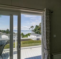 A patio door open to a balcony with chairs and a table overlooking houses trees and water at Bethany's Retreat in Wemyss Bay