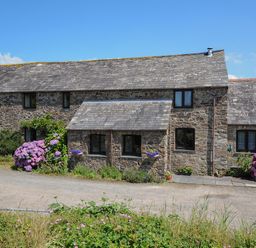 A stone house with multiple windows flowers and plants along the front and a clear sky at West Lee in Bude