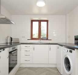 A kitchen with white cabinets black countertops a window sink oven washing machine and microwave at West Lee in Bude