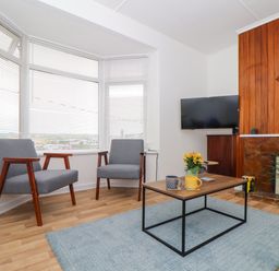 A sitting area with two grey chairs a wooden coffee table with mugs and flowers a wall-mounted TV and a fireplace at Small Hillman in Perranporth