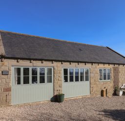 Stone cottage with three sets of windows and two planters on a gravel driveway at Roding Cottage in Egton