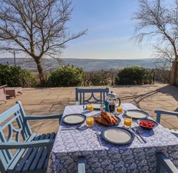 An outdoor patio with a table set for breakfast with plates croissants orange juice and strawberries at Roding Cottage Egton